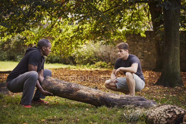 Personal Trainer zeigt jungen Mann, wie man Baumstamm im Park hebt — Stockfoto