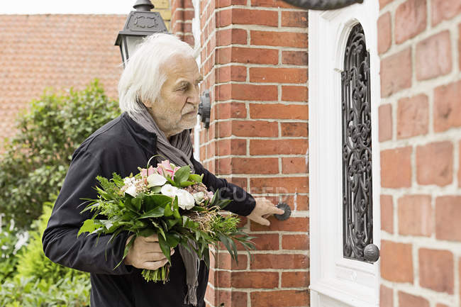 Старший мужчина с букетом звонит в дверь — стоковое фото