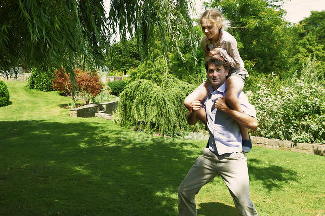 Homem maduro correndo com a filha em seus ombros no jardim — Fotografia de Stock