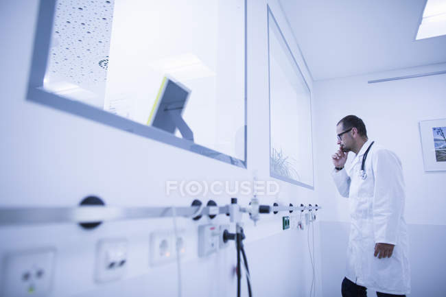 Врач наблюдает через окно в комнате для лечения в больнице — стоковое фото