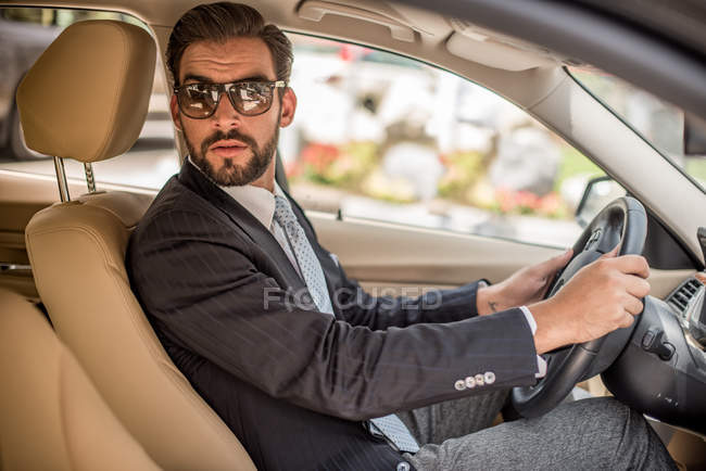 Young businessman driving car looking over his shoulder, Dubai, United Arab Emirates — Stock Photo
