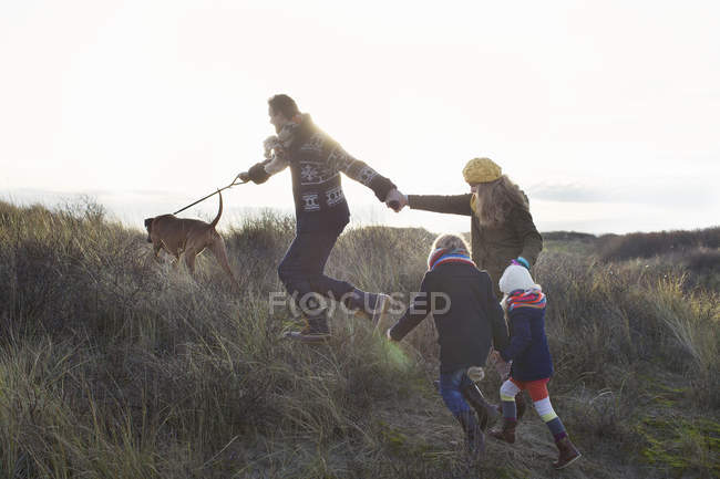 Mediados de pareja adulta paseando en dunas de arena con su hijo, hija y perro - foto de stock