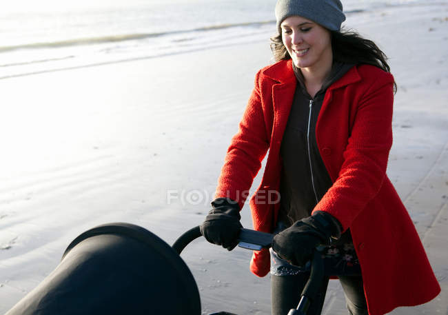Mother pushing stroller on beach — Stock Photo