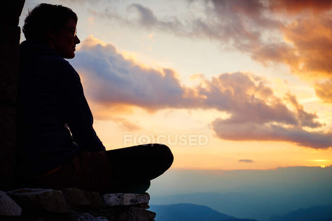 Силует жінки сидить хрест ноги дивитися захід сонця — стокове фото