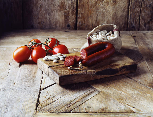 Vine tomatoes, chorizo and butter beans in burlap sack on wooden cutting board — Stock Photo