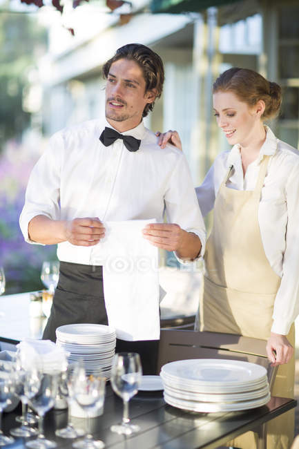 Camarero y camarera instalando mesas en el restaurante patio - foto de stock