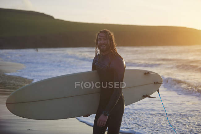 Portrait of young male surfer carrying surfboard on beach, Devon, England, UK — Stock Photo