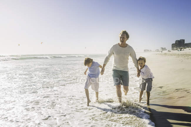 Padre e hijos tomados de la mano en la playa - foto de stock