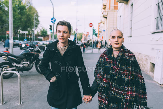 Молодая лесбийская пара, идущая по городской улице, держась за руки — стоковое фото