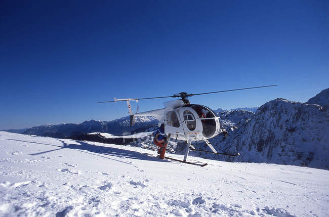 Skier climbing into helicopter on snow covered mountain — Stock Photo