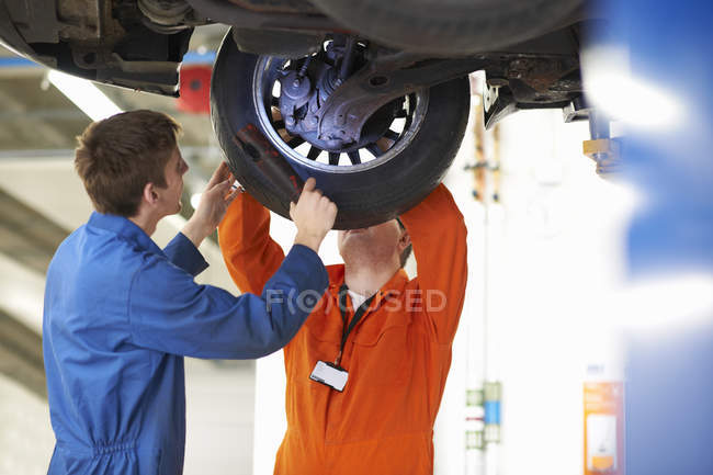 Estudiantes de mecánica universitaria inspeccionando rueda de coche en garaje de reparación - foto de stock