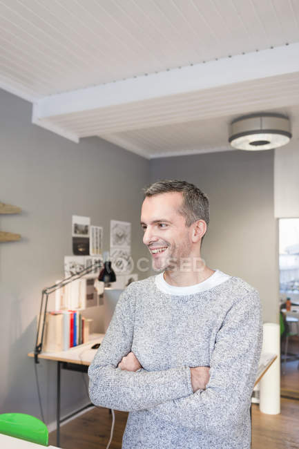 Mature man in office arms crossed looking away smiling — Stock Photo