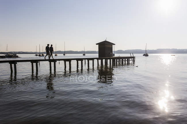 Silhouette eines Paares, das auf der Seebrücke zum Bootshaus läuft, schondorf, ammersee, Bayern, Deutschland — Stockfoto