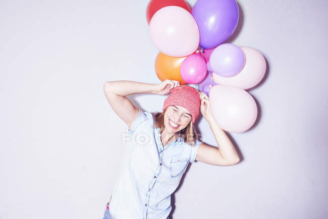 Estúdio tiro de mulher jovem segurando monte de balões na cabeça — Fotografia de Stock