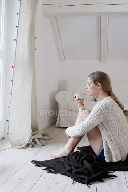 Mujer sentada en el suelo bebiendo té - foto de stock