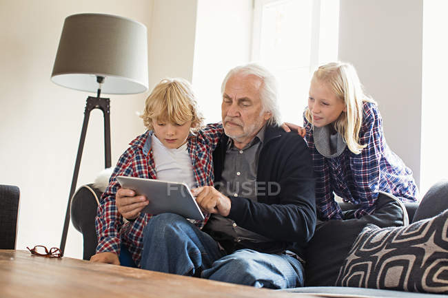 Abuelo usando tableta digital con nietos - foto de stock