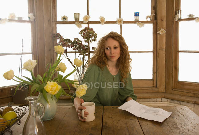 Woman drinking coffee at kitchen table — Stock Photo