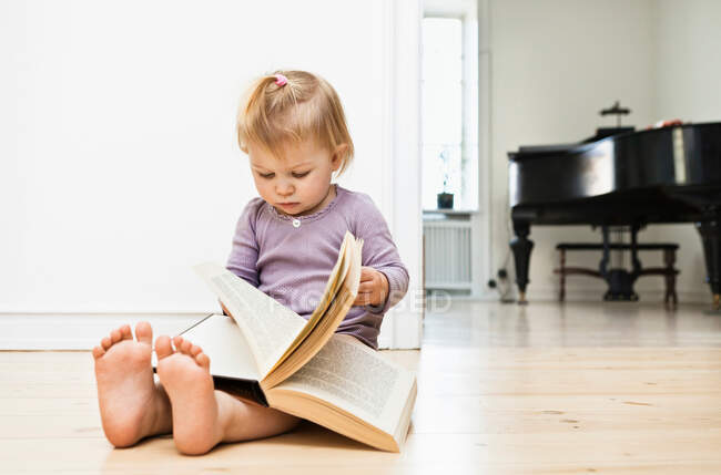Toddler girl sitting on floor reading book — Stock Photo