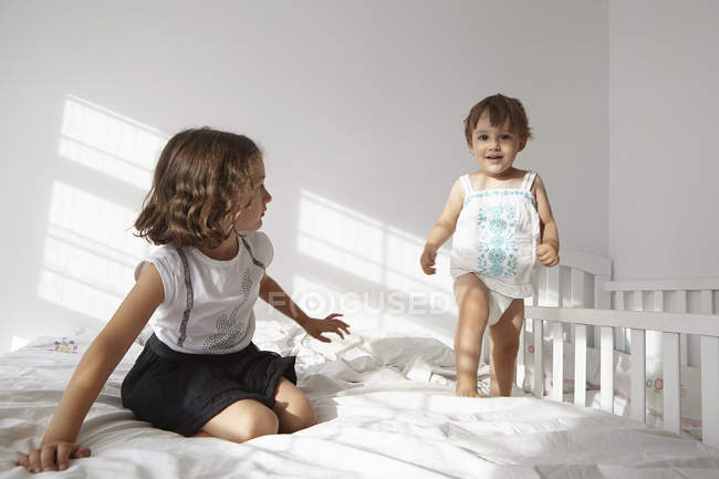 Mädchen beobachtet Kleinkind beim Gehen auf Bett — Stockfoto
