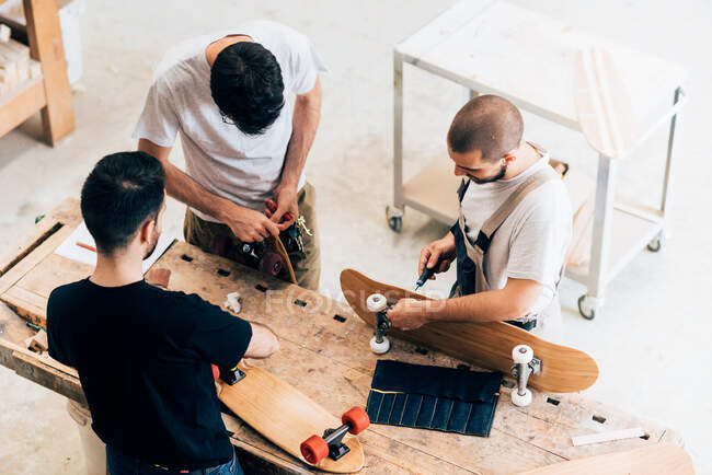 High angle view of young men standing around workbench attaching wheels to skateboards — Stock Photo