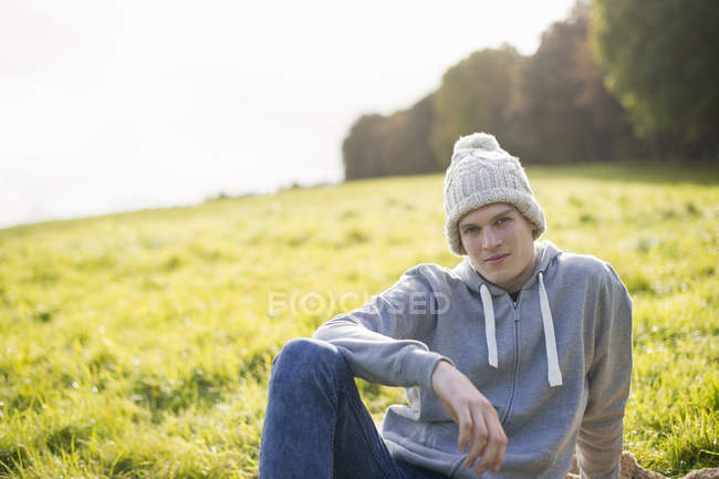 Retrato de jovem sentado na grama usando chapéu de malha — Fotografia de Stock