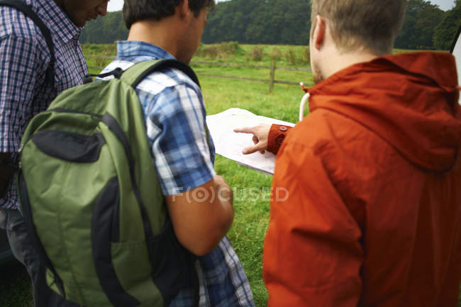 Tres excursionistas masculinos mirando el mapa al aire libre - foto de stock