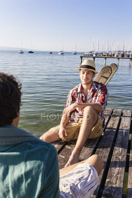 Friends sitting face to face on wood pier next to lake, Schondorf, Ammersee, Bavaria, Germany — Stock Photo
