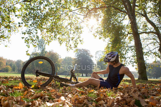 Cyclist looking at injury in the park — Stock Photo