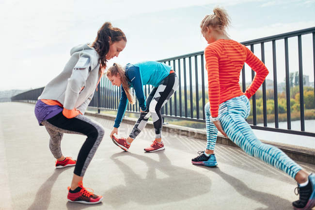 Tre corridori femminili che fanno esercizio di riscaldamento sul ponte pedonale — Foto stock
