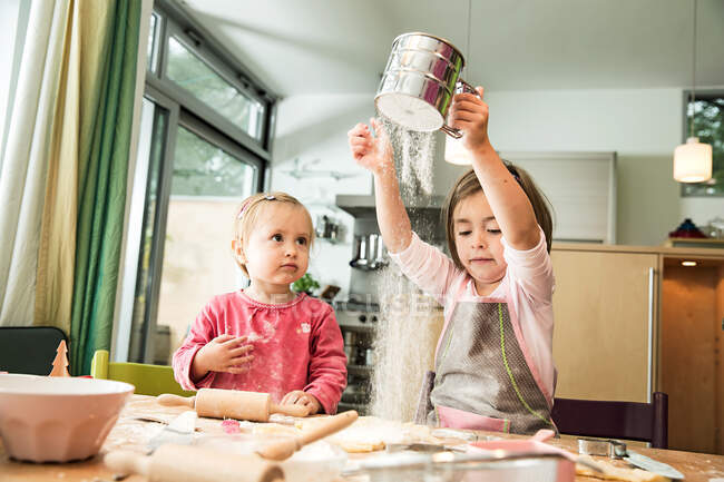 Menina peneirando farinha na cozinha — Fotografia de Stock