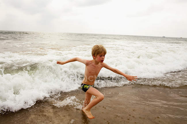 Junge spielt in Wellen am Strand — Stockfoto