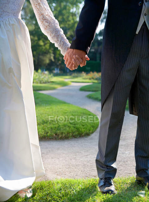 Bride and groom holding hands in garden — Stock Photo