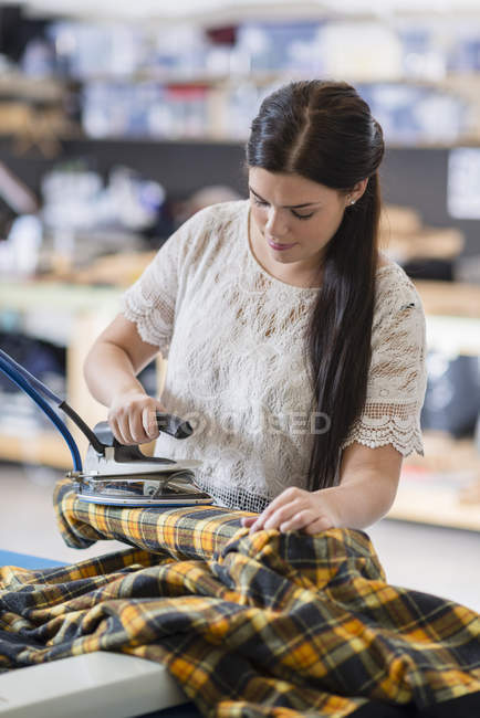 Jovem costureira passar tartan jaqueta na oficina — Fotografia de Stock