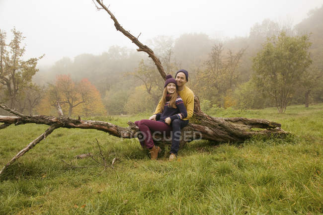 Young couple sitting on bare tree in misty park — Stock Photo