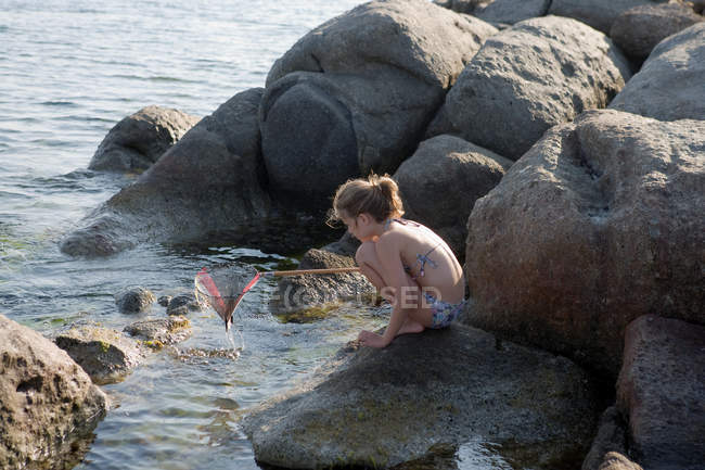 Chica joven agachada en las rocas y la pesca - foto de stock