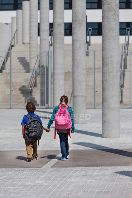Rear view of children holding hands and walking in courtyard — Stock Photo