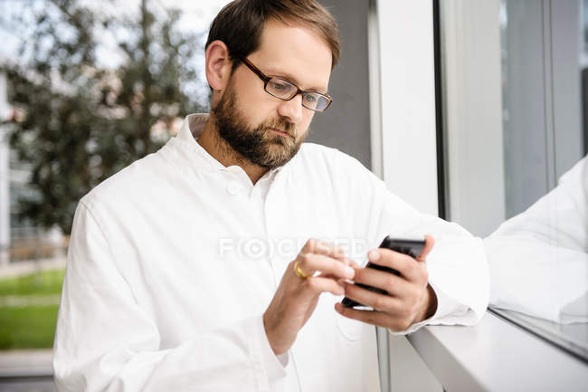 Doctor using cell phone at window — Stock Photo