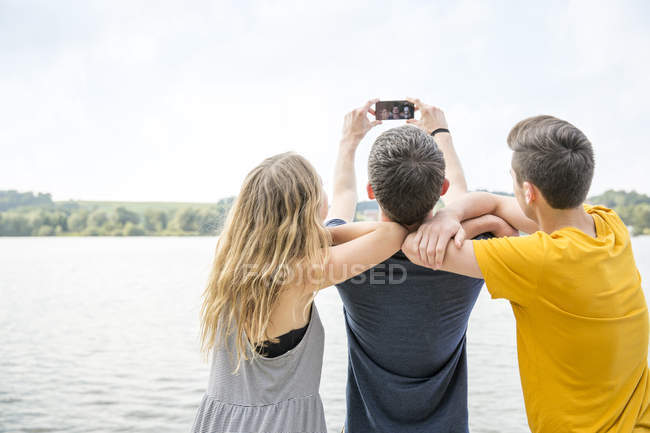 Троє молодих людей беруть автопортрет за допомогою смартфона, вид ззаду — стокове фото