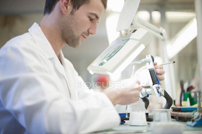 Technician using magnifier to repair denture — Stock Photo
