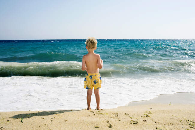 Joven niño de pie en la playa - foto de stock