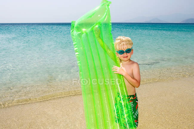 Jovem menino segurando colchão inflável na praia — Fotografia de Stock
