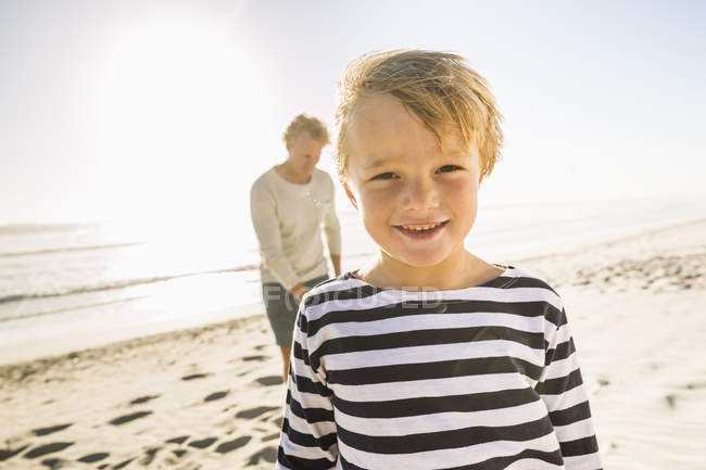 Retrato de niño en la playa con el padre mirando a la cámara sonriendo - foto de stock