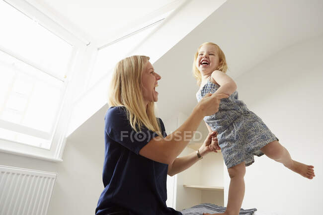 Mid adult woman and toddler daughter dancing on bed — Stock Photo