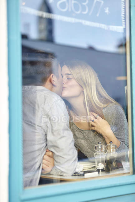 Romantic young couple at cafe window kissing — Stock Photo