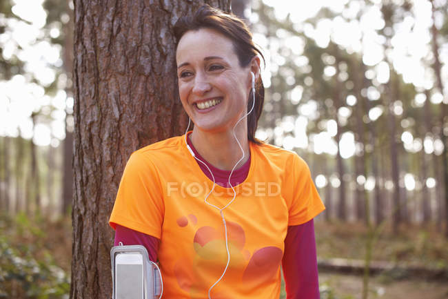 Mujer madura corredora con auriculares tomando un descanso en un bosque - foto de stock