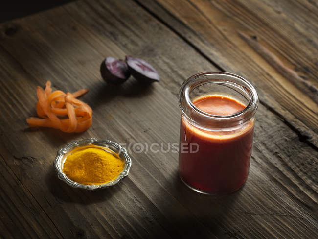 Suco cru de laranja em um jarro com beterraba, açafrão e cenoura ralada em madeira — Fotografia de Stock