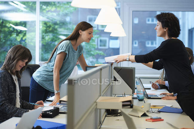 Businesswomen passing paperwork across screen partition in office — Stock Photo