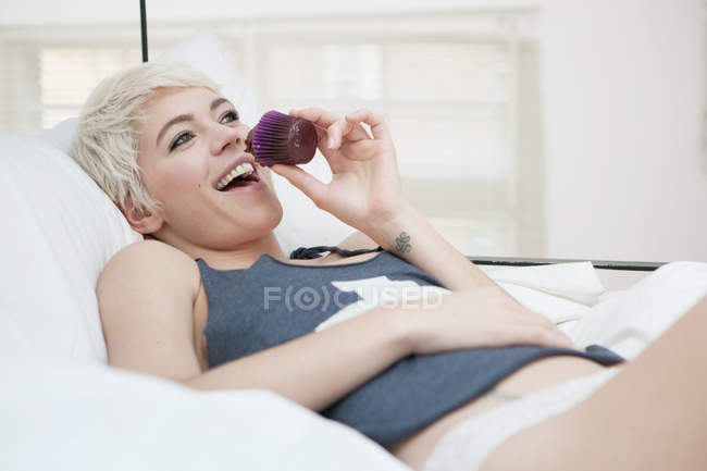 Woman lying on bed eating cupcake — Stock Photo