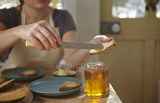 Женщина пробует свежевыжатый мед на хлебе, обрезанный кадр — стоковое фото