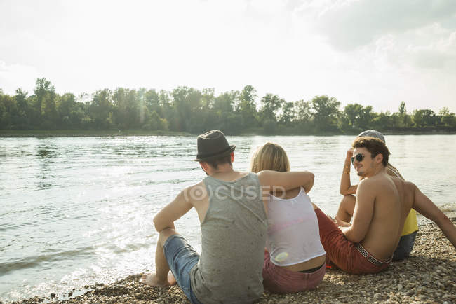 Чотири молодих друзі сидять на березі озера — стокове фото